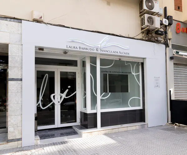 Fachada blanca de un centro de estética con logotipo en relieve y vinilos